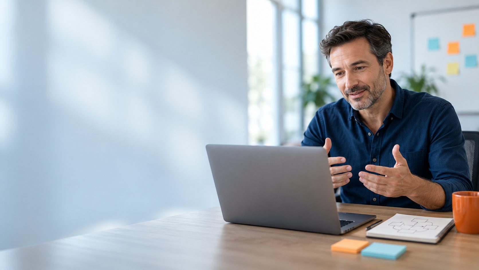 Ein Coach erklärt im Online-Coaching vor seinem Laptop etwas, daneben Notizblock mit Skizze und Haftnotizen